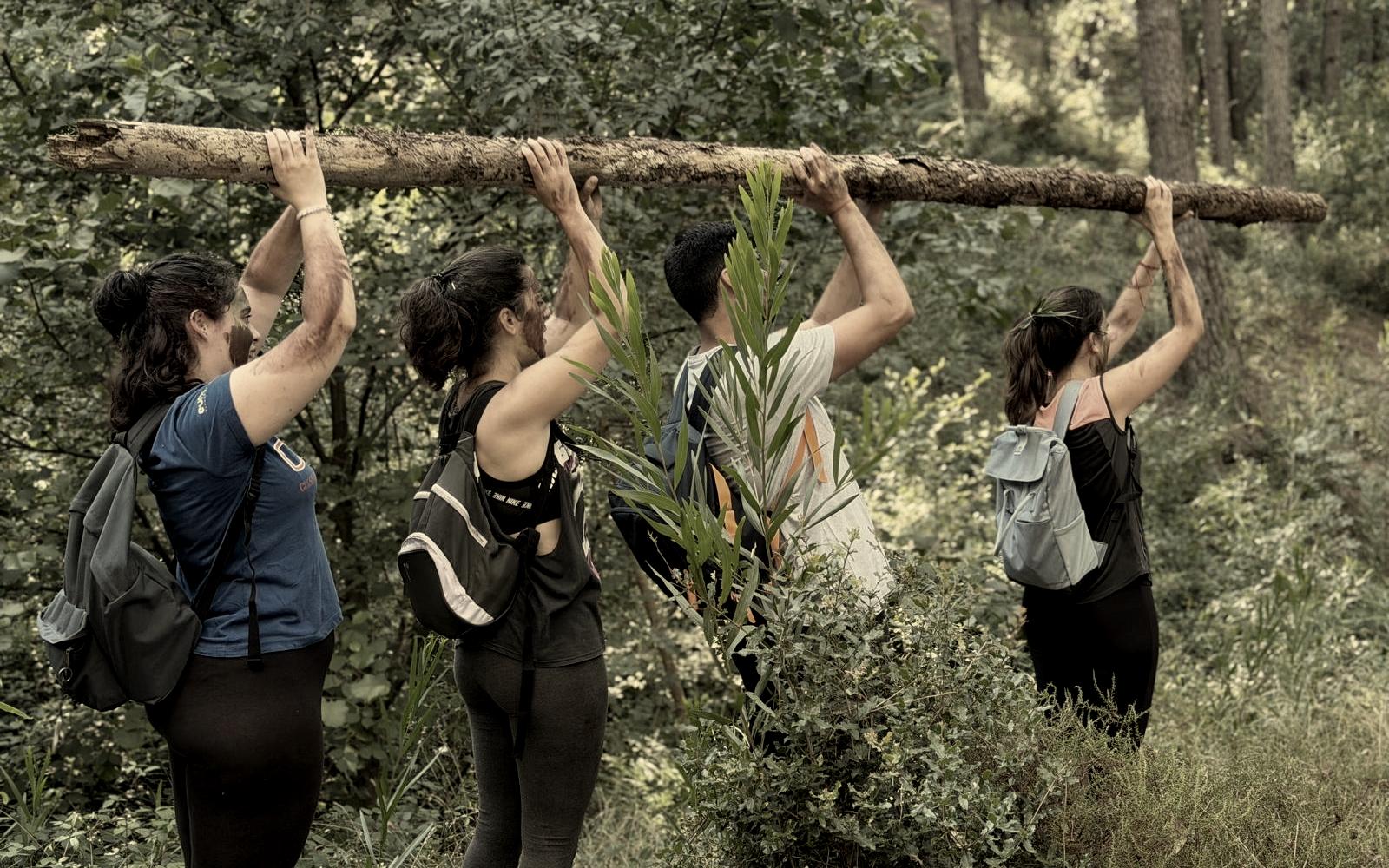 Equipa a carregar um tronco em conjunto, acima da cabeça, num exercício de cooperação